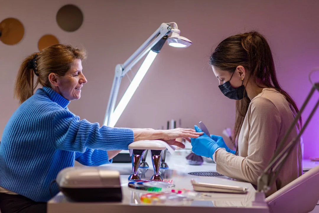 Manicura profesional en salón con mujer cliente y técnica aplicando esmalte con guantes y mascarilla