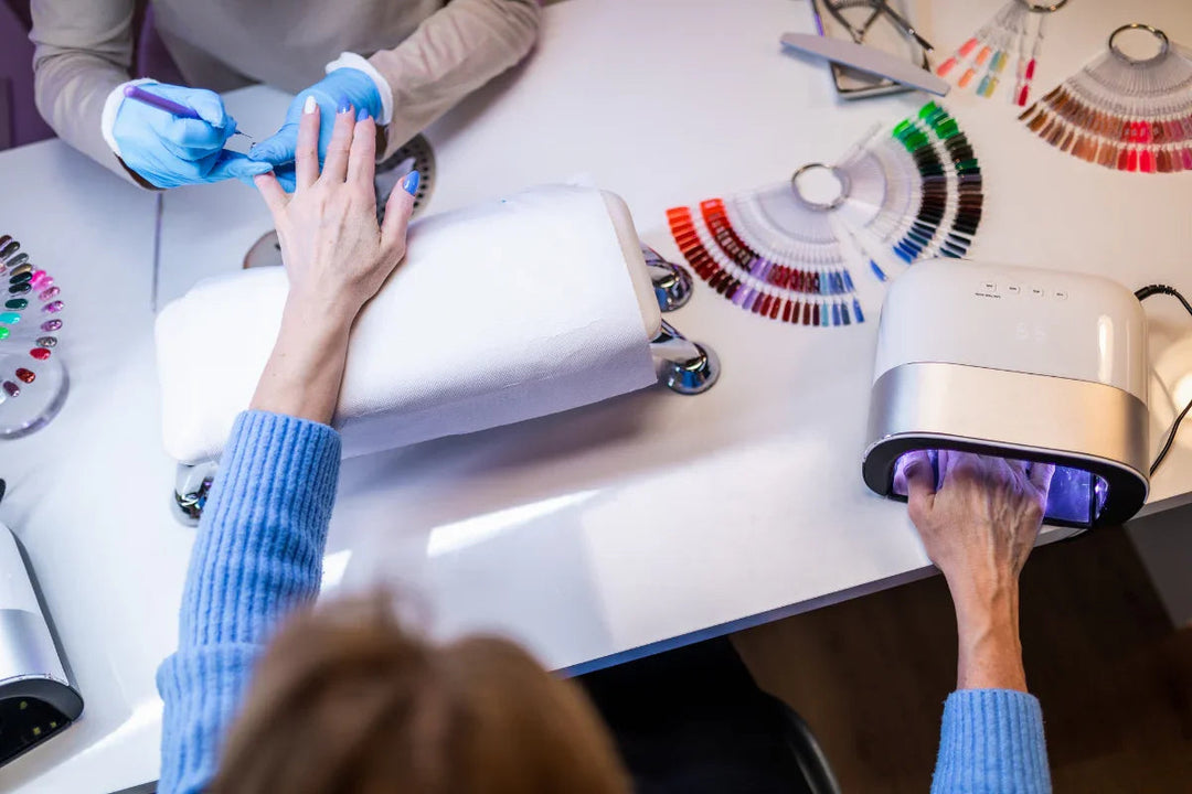 Manicura en salón de belleza con secado de uñas en lámpara LED y muestras de esmaltes