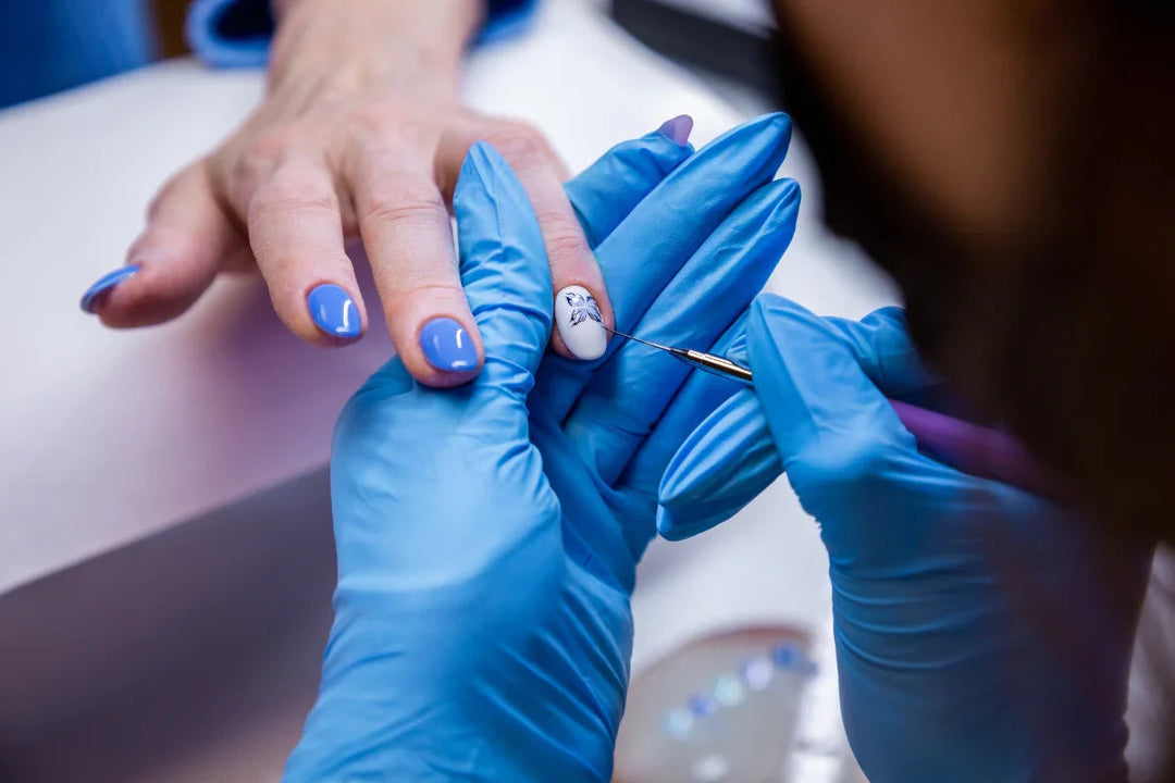 Manicura con uñas pintadas en azul y blanca, decoradas con arte floral detallado por técnico con guantes azules