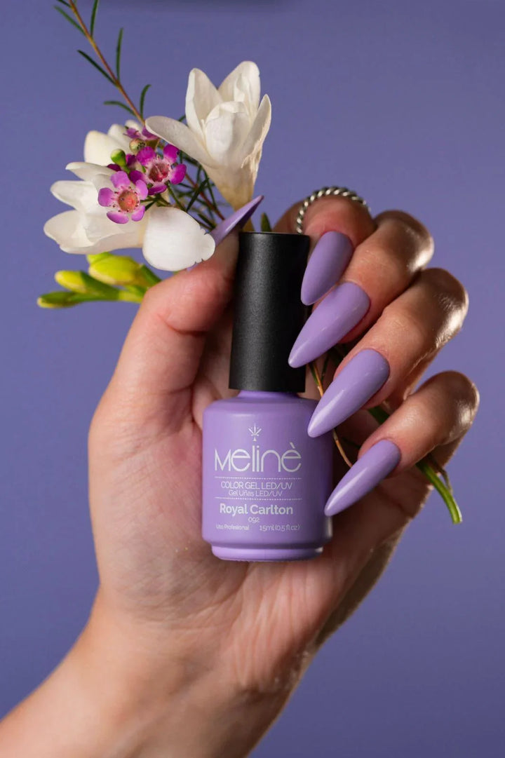 Mano con uñas largas en esmalte morado Meliné Royal Carlton sosteniendo flores blancas y moradas